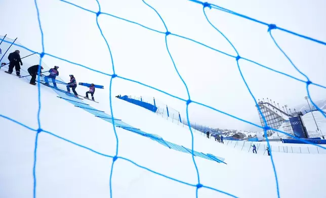 Workers set up fencing along the slopestyle course before a training session at the 2026 Winter Olympics, in Livigno, Italy, Wednesday, Feb. 4, 2026. (AP Photo/Gregory Bull)