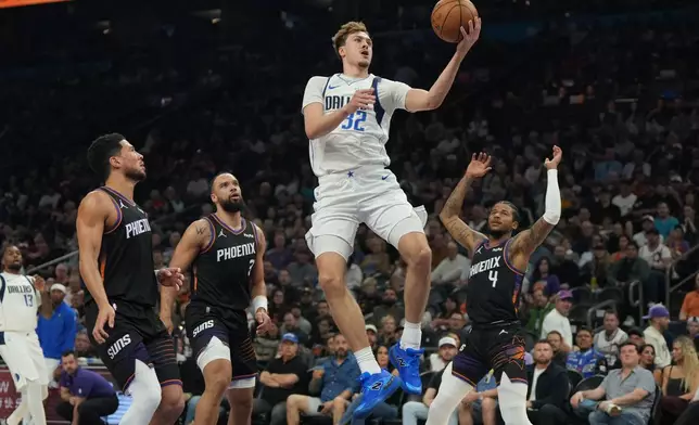 Dallas Mavericks forward Cooper Flagg scores between Phoenix Suns guard Devin Booker, forward Dillon Brooks (3), and guard Jalen Green (4) during the first half of an NBA basketball game, Tuesday, Feb. 10, 2026, in Phoenix. (AP Photo/Rick Scuteri)