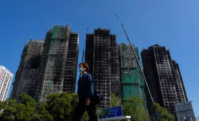 A pedestrian walks past the fire-ravaged residential towers of the Wang Fuk Court apartment complex, in the Tai Po district of Hong Kong, Friday, Feb. 6, 2026. (AP Photo/Chan Long Hei)