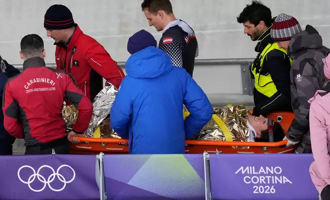 Team members and rescue workers carry an injured athlete after Austria's team Jakob Mandlbauer, Daniel Bertschler, Sebastian Mitterer and Daiyehan Nichols-Bardi crashed during a four man bobsled run at the 2026 Winter Olympics, in Cortina d'Ampezzo, Italy, Saturday, Feb. 21, 2026. (AP Photo/Aijaz Rahi)