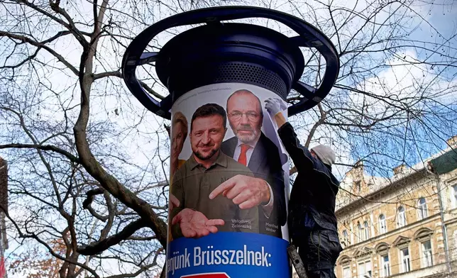 A man fixes a partially damaged billboard showing an AI-generated image of Ukrainian President Volodymyr Zelenskyy, center, flanked by European officials, in Budapest, Hungary, Monday, Feb. 23, 2026. (AP Photo/Bela Szandelszky)