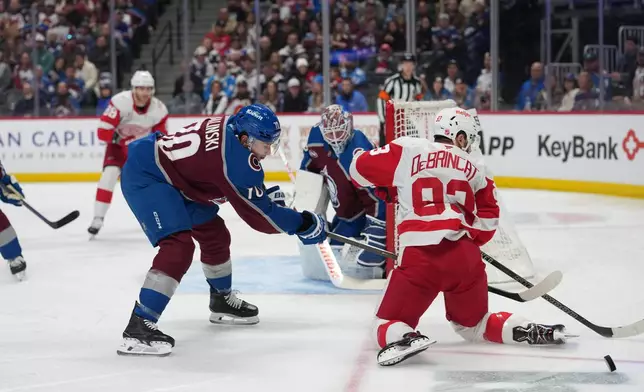 Detroit Red Wings right wing Alex DeBrincat, right, struggles to control the puck as Colorado Avalanche defenseman Sam Malinski, front left, covers in the second period of an NHL hockey game Monday, Feb. 2, 2026, in Denver. (AP Photo/David Zalubowski)