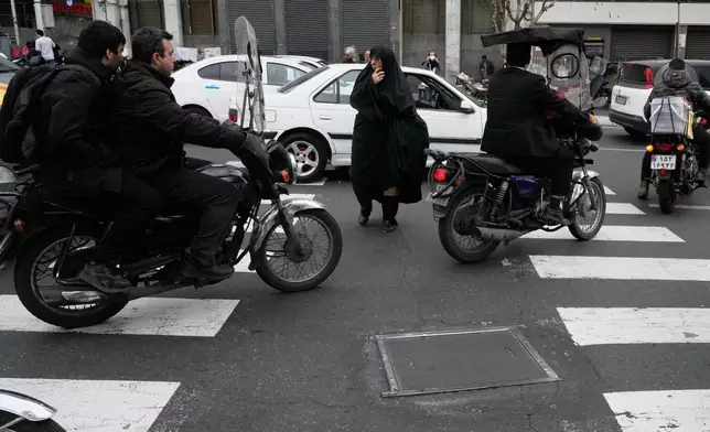 A woman crosses a square as motorbikes ride past in downtown Tehran, Iran, Tuesday, Feb. 24, 2026. (AP Photo/Vahid Salemi)