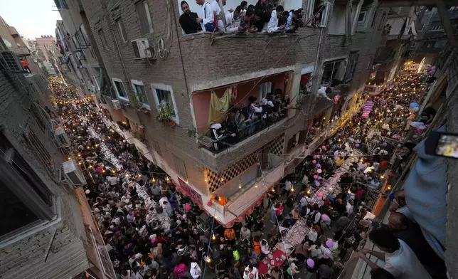 FILE - Residents of Ezbet Hamada in Cairo's El Matareya district peer from their balconies to celebrate a mass break-fast, "Iftar" during the holy fasting month of Ramadan in Cairo, March 15, 2025. (AP Photo/Amr Nabil, File)