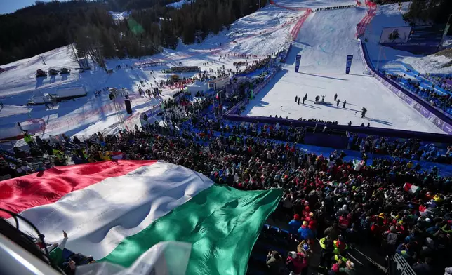 A giant Italian flag is displayed by fans during the medal ceremony where Italy's Federica Brignone won the gold medal in an alpine ski, women's giant slalom race, at the 2026 Winter Olympics, in Cortina d'Ampezzo, Italy, Sunday, Feb. 15, 2026. (AP Photo/Andy Wong)