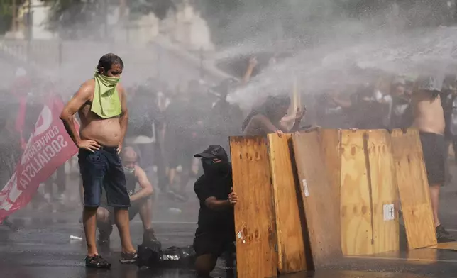 Protesters shield themselves with wooden boards as police spray water during clashes at a march by trade unions and opposition groups against a labor reform bill proposed by President Javier Milei's government in Buenos Aires, Argentina, Wednesday, Feb. 11, 2026. (AP Photo/Rodrigo Abd)