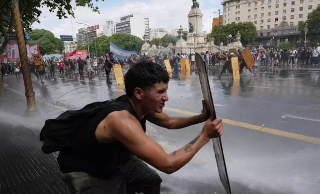 Protesters shield themselves with wooden boards as police spray water during clashes at a march by trade unions and opposition groups against a labor reform bill proposed by President Javier Milei's government in Buenos Aires, Argentina, Wednesday, Feb. 11, 2026. (AP Photo/Rodrigo Abd)