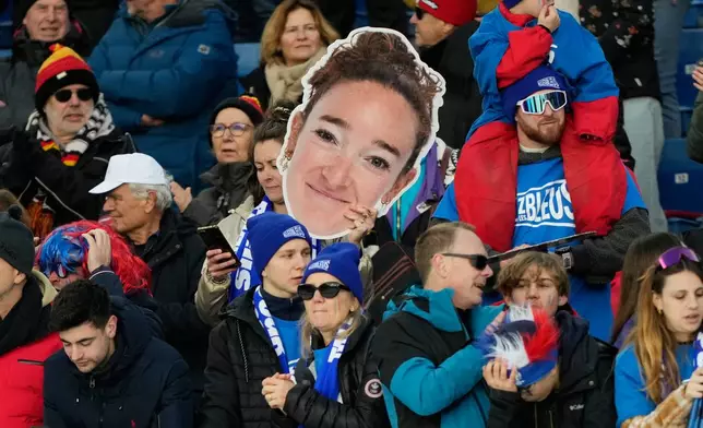 A fan holds an image of France's Lou Jeanmonnot, gold medalist in the 4X6-kilometer mixed relay biathlon race at the 2026 Winter Olympics in Anterselva, Italy, Sunday, Feb. 8, 2026. (AP Photo/Mosa'ab Elshamy)
