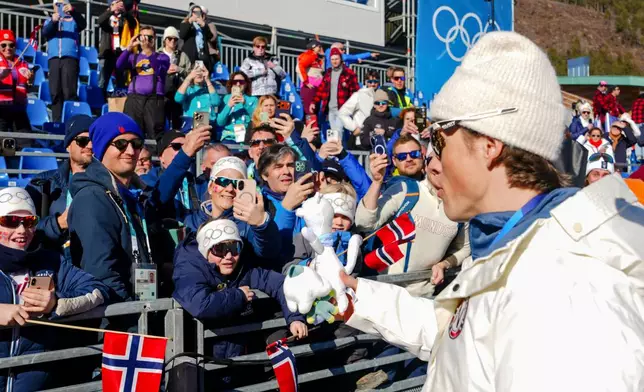 Johannes Hoesflot Klaebo, of Norway, gives his Tina mascot tooth to fans on the stands after winning the gold medal in the cross country skiing men's 4 x 7.5km relay at the 2026 Winter Olympics, in Tesero, Italy, Sunday, Feb. 15, 2026. (AP Photo/Kirsty Wigglesworth)