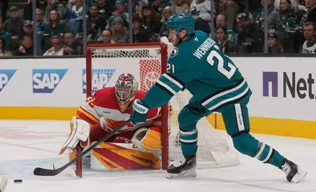 San Jose Sharks center Alexander Wennberg (21) reaches for the puck against Calgary Flames goaltender Dustin Wolf (32) during the first period of an NHL hockey game in San Jose, Calif., Thursday, Feb. 26, 2026. (AP Photo/Jeff Chiu)