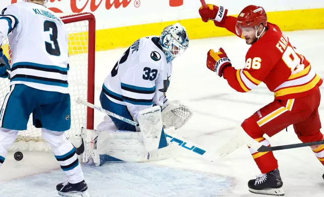 Calgary Flames' Joel Farabee, right, scores on San Jose Sharks goalie Alex Nedeljkovic as John Klingberg looks on during the third period of an NHL hockey game in Calgary, Saturday, Jan. 31, 2026. (Larry MacDougal/The Canadian Press via AP)