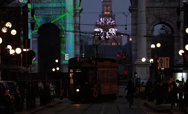 A traditional vintage trams travel on rails through a downtown street near to the Peace Arch, with a view of the Olympic cauldron in the background, ahead of the 2026 Winter Olympics, in Milan, Italy, Saturday, Jan. 31, 2026. (AP Photo/Luca Bruno)
