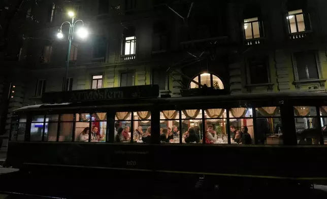 People eat dinner in the 'ATMosfera' restaurant traditional vintage tram traveling on rails through a downtown street, in Milan, Italy, Monday, Dec. 15, 2025. (AP Photo/Luca Bruno)