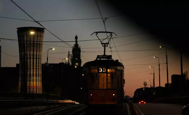 A traditional vintage tram travels on rails near to the Rainbow Tower, a former water tank, through a downtown street, in Milan, Italy, Saturday, Nov. 29, 2025. (AP Photo/Luca Bruno)