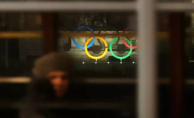 A woman sits in a traditional vintage tram traveling through a downtown street as it passes by Olympic rings placed in front of the town hall, in Milan, Tuesday, Dec. 2, 2025. (AP Photo/Luca Bruno)