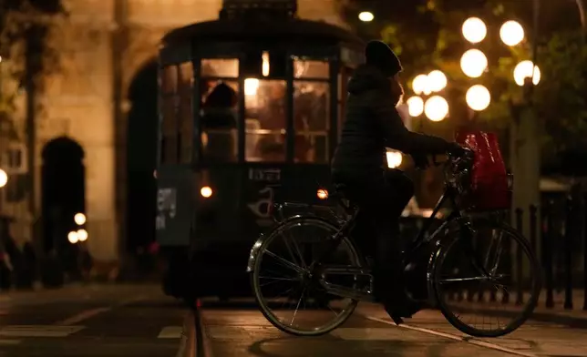 A woman rides her bike past a traditional vintage tram near to the Peace Arch, in Milan, Italy, Saturday, Nov. 29, 2025. (AP Photo/Luca Bruno)