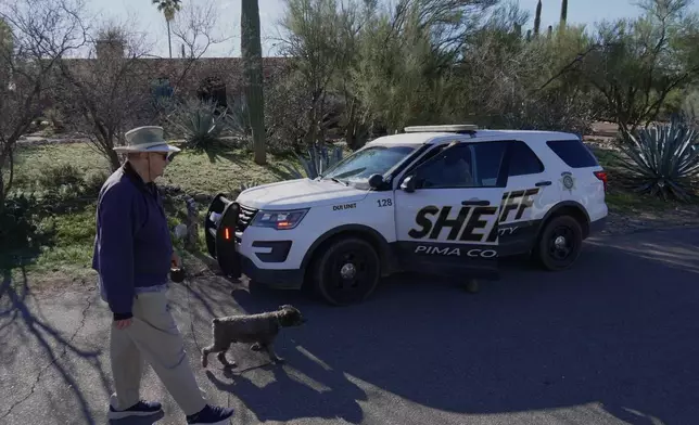 A person walks a dog as members of the Pima County sheriffs office remains outside of Nancy Guthrie's home, Monday, Feb. 9, 2026 in Tucson, Ariz. (AP Photo/Ty ONeil)