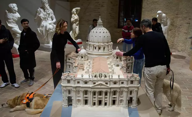 Stefania Terre, left, and Carmine Laezza, far right, both blind, touch a reproduction of St. Peter's Basilica at the Omero Tactile Museum in Ancona, Italy, Thursday, Jan. 15, 2026. (AP Photo/Alessandra Tarantino)