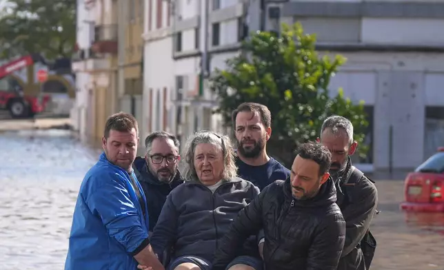 Iria Afonso, 76, is carried on a chair by neighbors as she is evacuated from her flooded home after heavy rains caused the Sado River to overflow in Alcácer do Sal, southern Portugal, Friday, Feb. 6, 2026. (AP Photo/Ana Brigida)