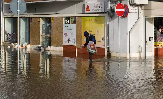A man walks along a flooded street after the Sado River overflowed following heavy rains in Alcácer do Sal, southern Portugal, Friday, Feb. 6, 2026. (AP Photo/Ana Brigida)
