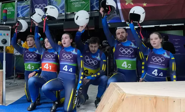 Ukraine's Yulianna Tunytska, Olena Stetskiv, Oleksandra Mokh, Nazarii Kachmar, Ihor Hoi and Andriy Mandziy kneel down during the luge relay competition at the 2026 Winter Olympics, in Cortina d'Ampezzo, Italy, Thursday, Feb. 12, 2026. (AP Photo/Alessandra Tarantino)