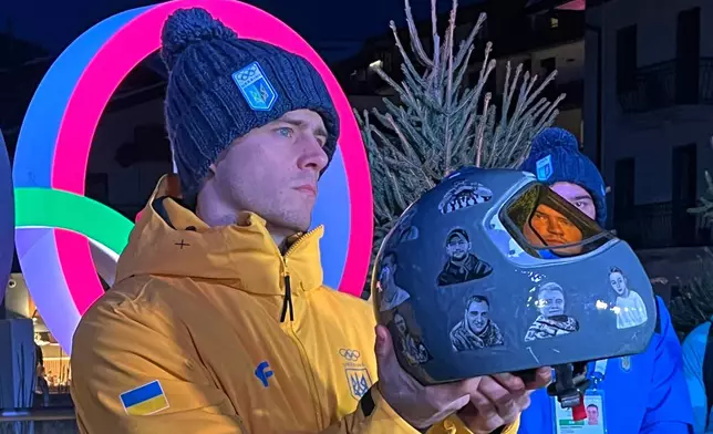 Ukraine's Vladyslav Heraskevych holds up his crash helmet during a press conference following a skeleton training session at the 2026 Winter Olympics, in Cortina d'Ampezzo, Italy, Tuesday, Feb. 10, 2026. (AP Photo/Steve Moore)