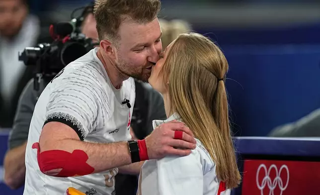 Switzerland's Yannick Schwaller and Briar Schwaller-Huerlimann kiss during the mixed doubles round robin phase of the curling competition against Britain, at the 2026 Winter Olympics, in Cortina d'Ampezzo, Italy, Sunday, Feb. 8, 2026. (AP Photo/Fatima Shbair)