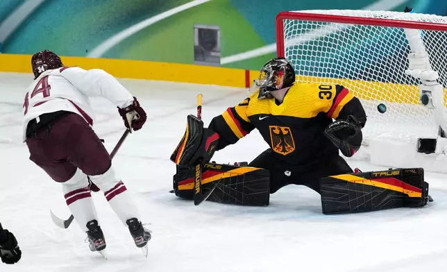 Latvia's Eduards Tralmaks (34) scores against Germany goalkeeper Philipp Grubauer (30) during the third period of a men's ice hockey preliminary round match at the 2026 Winter Olympics, in Milan, Italy, Saturday, Feb. 14, 2026. (AP Photo/Carolyn Kaster)