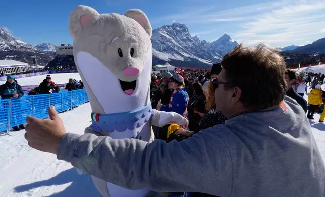 A spectator moves in to hug Olympic mascot Tina prior to an alpine ski women's downhill race, at the 2026 Winter Olympics, in Cortina d'Ampezzo, Italy, Sunday, Feb. 8, 2026.. (AP Photo/Robert F. Bukaty)