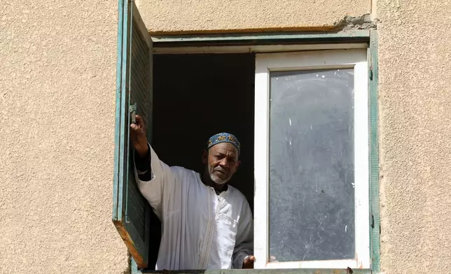 Farouk Abkar, a 60-year-old former charity kitchen worker who spent a year distributing grain and organizing lines at a charity kitchen in Zam Zam refugee camp in Sudan, peers from his home window in 6 October city, Egypt, Wednesday, Jan. 28, 2026. (AP Photo/Khaled el Fiqi)