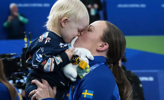 Sweden's Sofia Scharback holds her child after winning the gold medal of the women's curling, at the 2026 Winter Olympics, in Cortina d'Ampezzo, Italy, Sunday, Feb. 22, 2026.(AP Photo/Misper Apawu)