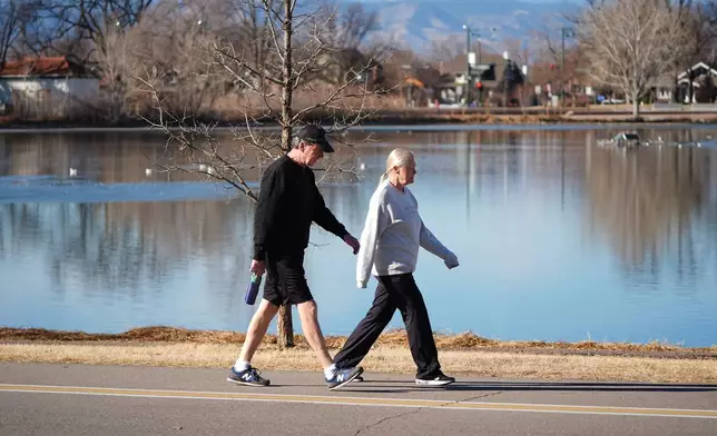 With a backdrop of snowless mountains, a couple walk around the lake in Washington Park, Friday, Feb. 6, 2026, in Denver. (AP Photo/David Zalubowski)
