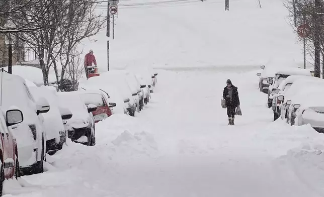 FILE - A person carries grocery bags up a residential street during a winter storm Jan. 25, 2026, in Cincinnati. (AP Photo/Joshua A. Bickel, File)