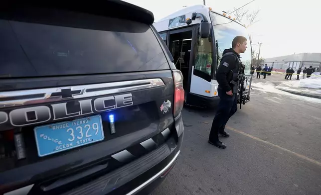 A police officer stands in front of a public transit bus that was used to bus hockey players away from the Lynch Arena in Pawtucket, R.I., after a shooting at the ice rink, Monday, Feb. 16, 2026. (AP Photo/Mark Stockwell)