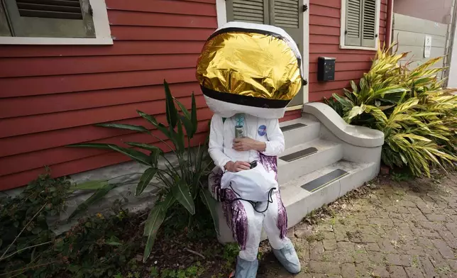 A person participating in the Society of Saint Anne parade sits on a front stoop of a buidling during Mardi Gras Day, Tuesday, Feb. 17, 2026 in New Orleans. (AP Photo/Matthew Hinton)