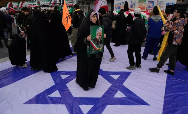 A woman holds a poster of the late commander of Iran's Revolutionary Guard expeditionary Quds Force, Gen. Qassem Soleimani, who was killed in a U.S. drone attack in 2020 in Iraq, as she stands on a banner containing an image of the Israeli flag in an annual rally marking 1979 Islamic Revolution at the Azadi, or Freedom, Street in Tehran, Iran, Wednesday, Feb. 11, 2026. (AP Photo/Vahid Salemi)