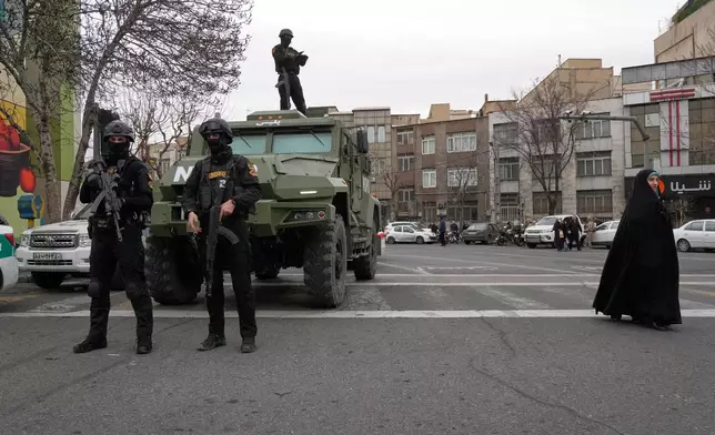 Policemen stand guard during an annual rally marking 1979 Islamic Revolution as a woman walks at right at the Azadi (Freedom) St. Tehran, Iran, Wednesday, Feb. 11, 2026. (AP Photo/Vahid Salemi)