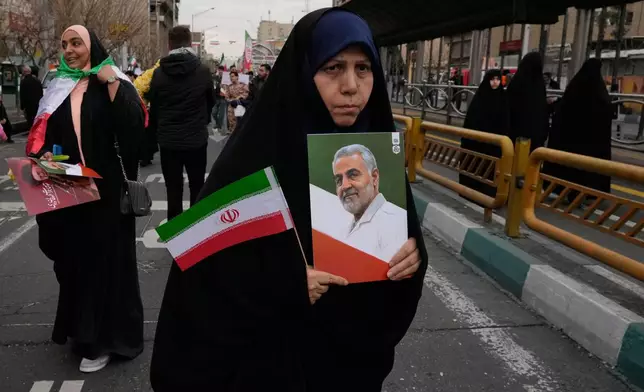 A woman carries an Iranian flag and a picture of the late commander of the Revolutionary Guard aerospace division Gen. Amir Ali Hajizadeh, who was killed in an Israeli strike in June 2025, during an annual rally marking 1979 Islamic Revolution at the Azadi, Freedom, Street in Tehran, Iran, Wednesday, Feb. 11, 2026. (AP Photo/Vahid Salemi)