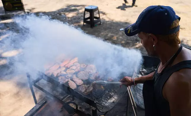 Cesar Tousedo grills meat to sell at a street stall in Buenos Aires, Argentina, Tuesday, Feb. 10, 2026. (AP Photo/Rodrigo Abd)