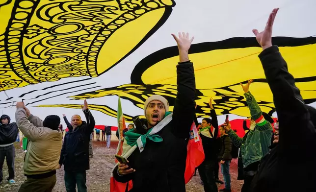 Supports of Iran's exiled Crown Prince Reza Pahlavi stand under a huge historic Iranian flag as they attend a demonstration during the Munich Security Conference in Munich, Germany, Saturday, Feb. 14, 2026. (AP Photo/Ebrahim Noroozi)