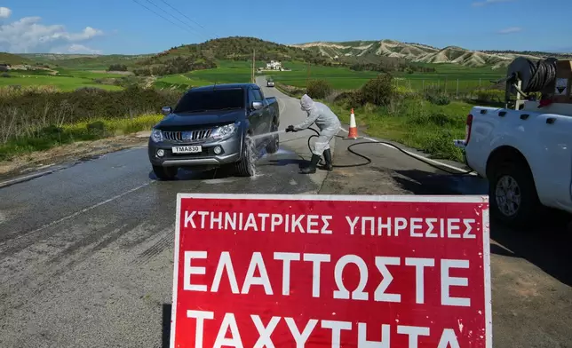 An employee sprays a car inside a blocked section of a livestock zone containing thousands of goats, sheep, and cows following an outbreak of foot-and-mouth disease in the Troulloi area near Larnaca, Cyprus, Wednesday, Feb. 25, 2026. (AP Photo/Petros Karadjias)