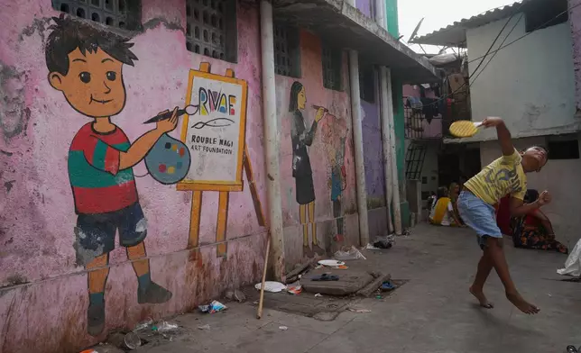 A boy plays near a wall of public toilet that shows a mural by the Rouble Nagi Art Foundation in the Dhobi Ghat area of Mumbai, India, Thursday, Feb. 5, 2026.(AP Photo/Rafiq Maqbool)