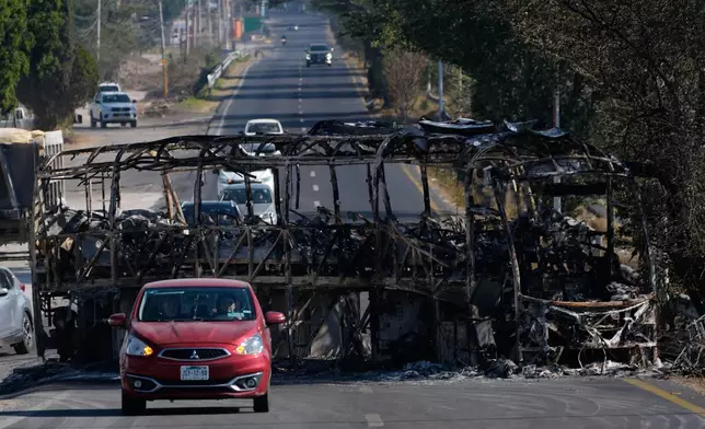 Vehicles drive past a charred bus the day after the Mexican army killed Jalisco New Generation Cartel leader Nemesio Oseguera Cervantes, known as "El Mencho," in Guadalajara, Mexico, Monday, Feb. 23, 2026. (AP Photo/Marco Ugarte)