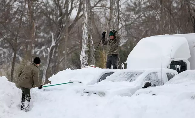 Men clear snow off of cars and trucks in a parking lot, Monday, Feb. 23, 2026, in St. James, N.Y. (AP Photo/Heather Khalifa)
