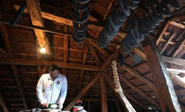 Misa Rajic irons sausage using a glass bottle in the attic of his home in Pirot, Serbia, on Feb. 13, 2026. (AP Photo/Darko Vojinovic)