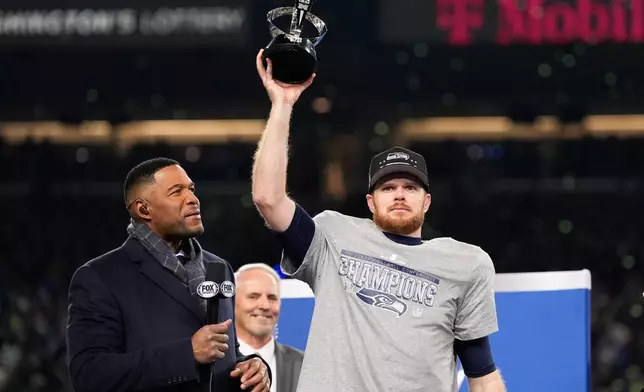 Seattle Seahawks quarterback Sam Darnold lifts the winner's trophy next to Michael Strahan, left, after a win over the Los Angeles Rams in the NFC Championship NFL football game Sunday, Jan. 25, 2026, in Seattle. (AP Photo/Godofredo A. Vásquez)