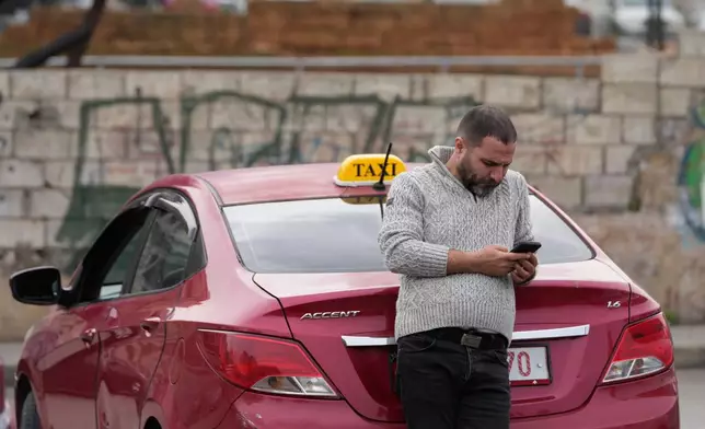 A taxi driver who blocks a main highway with his car, checks his mobile phone during a protest against the increased taxes and gasoline prices issued by the Lebanese Cabinet on Monday, in Beirut, Lebanon, Tuesday, Feb. 17, 2026. (AP Photo/Hussein Malla)