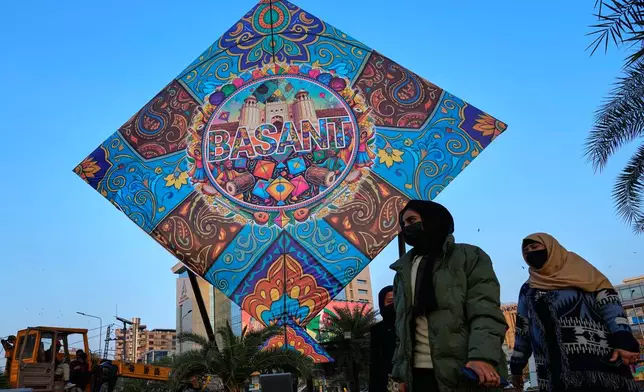 Women walk past a giant kite model placed by local administration to celebrate the upcoming three-day kite flying festival 'Basant' in Lahore, Pakistan, Wednesday, Feb. 4, 2026. (AP Photo/K.M. Chaudary)