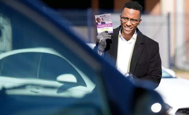 Texas Congressional Candidate Christian D. Menefee holds up one of his flyers as a voter passes by in a car while he visited a polling location at Acres Homes MultiService Center on Election Day, in Houston, Saturday, Jan. 31, 2026. (AP Photo/ Karen Warren)