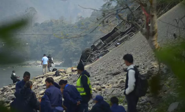 The wreckage of a bus is seen on the bank of the Trishuli River after it drove off a mountain highway near Benighat, west of the capital, Kathmandu, Nepal, Monday, Feb. 23, 2026. (AP Photo/Bijay Rai)